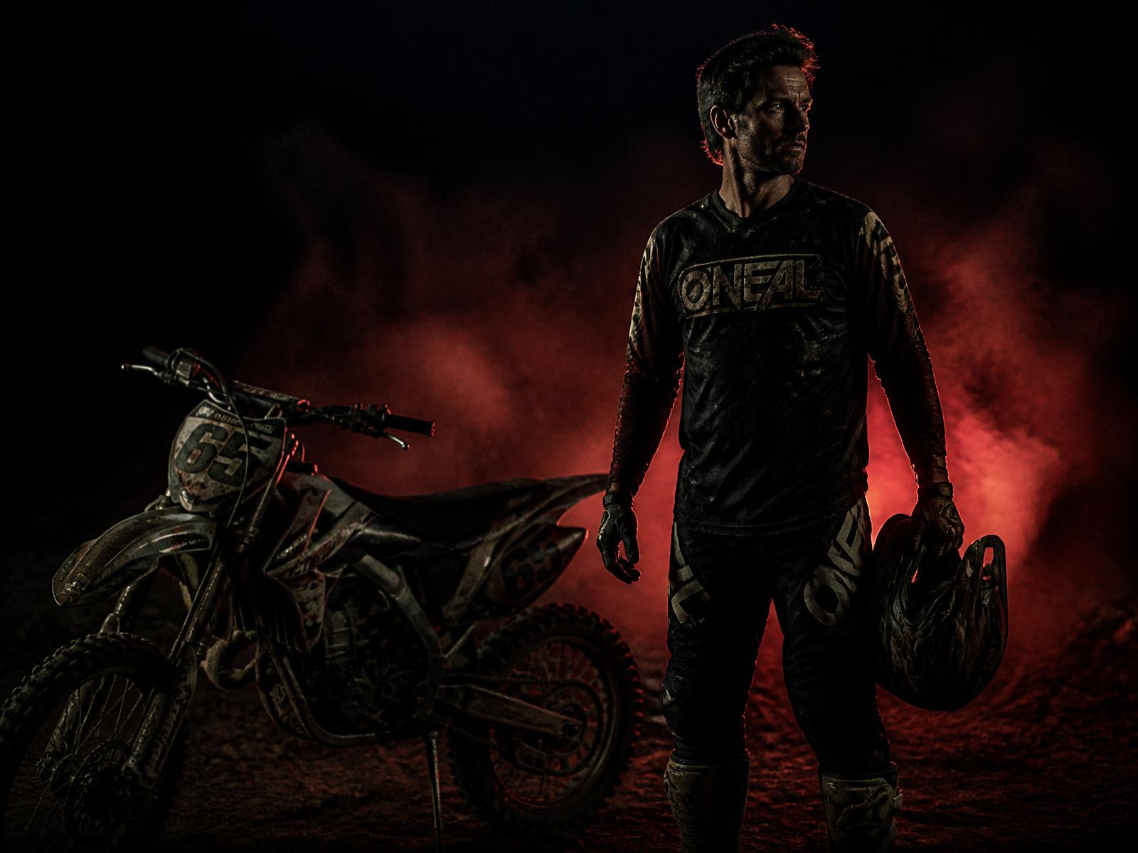 Motocross rider standing beside his bike at dusk